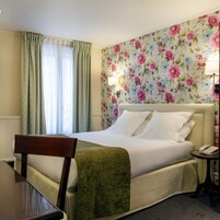 Une chambre d’hôtel avec un lit, une chaise, une table de chevet avec une lampe et un papier peint à motifs floraux.