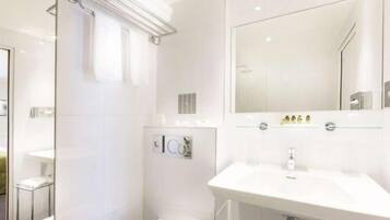 A modern bathroom with a glass shower enclosure, a large mirror above the sink, and a toilet with a glass partition.