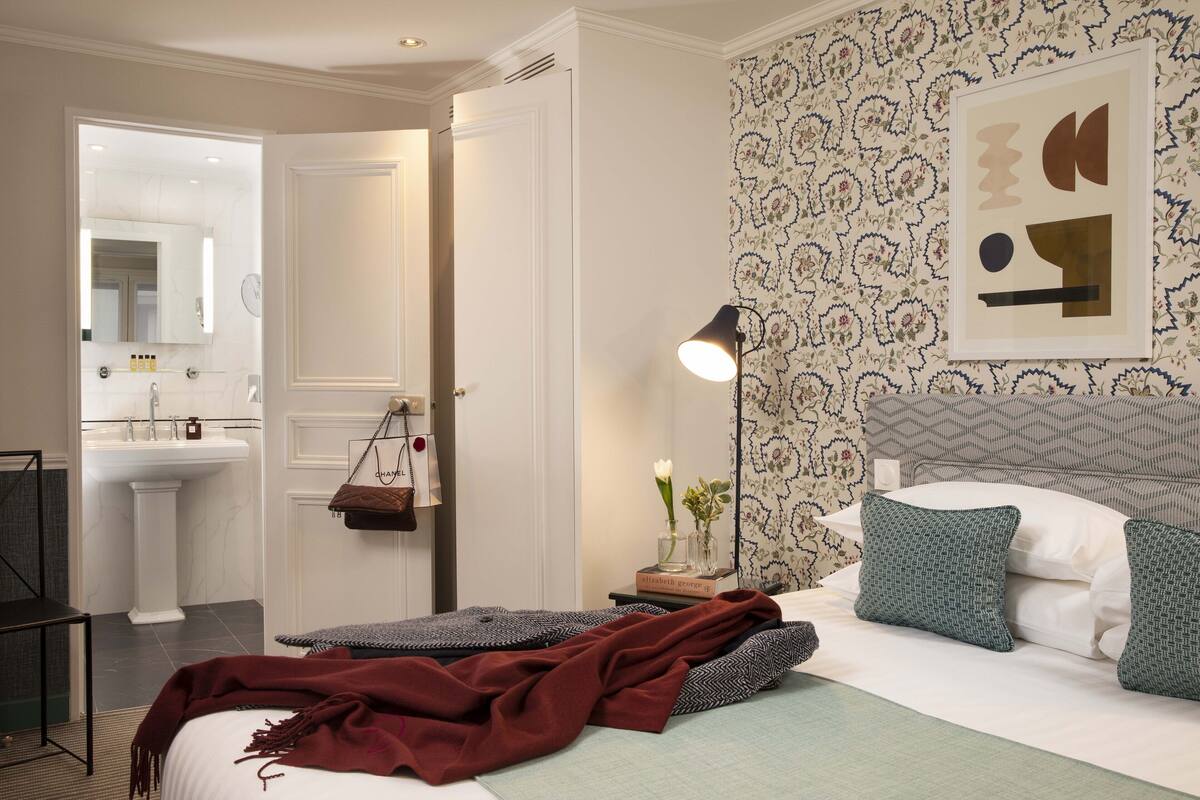 A bedroom with a bed, bedside table, lamp, and a view of the bathroom.