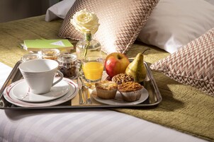A breakfast tray with a cup, juice, apple, pear, muffins, and a bottle on a bed with patterned pillows.
