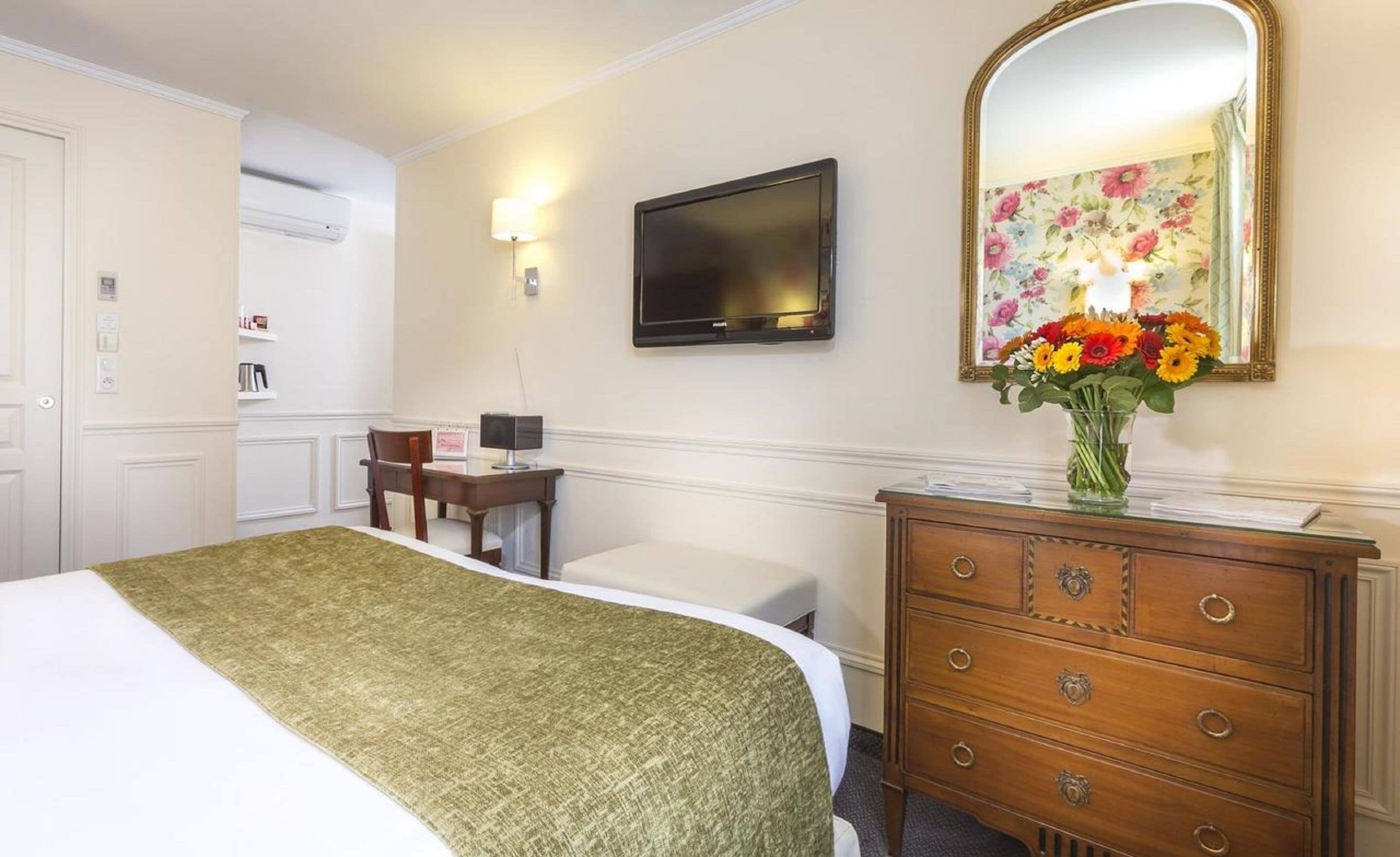 Een hotelkamer met een bed, een bureau, een dressoir, een televisie en een spiegel met bloemenmotief.