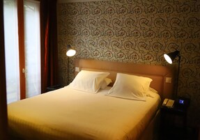 A hotel room with a bed, two bedside lamps, a telephone, and a patterned wallpaper.