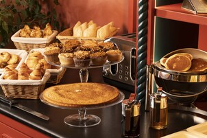 A buffet table with various baked goods including pastries, muffins, and a cake.