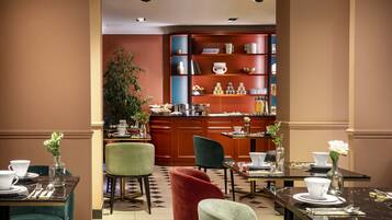 Een hotel lobby met een bar, zitplaatsen met tafels klaar voor dineren, en een grote boekenkast vol boeken en decoratieve objecten.