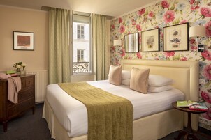 A hotel room with a bed, a dresser, a window with curtains, and floral wallpaper.