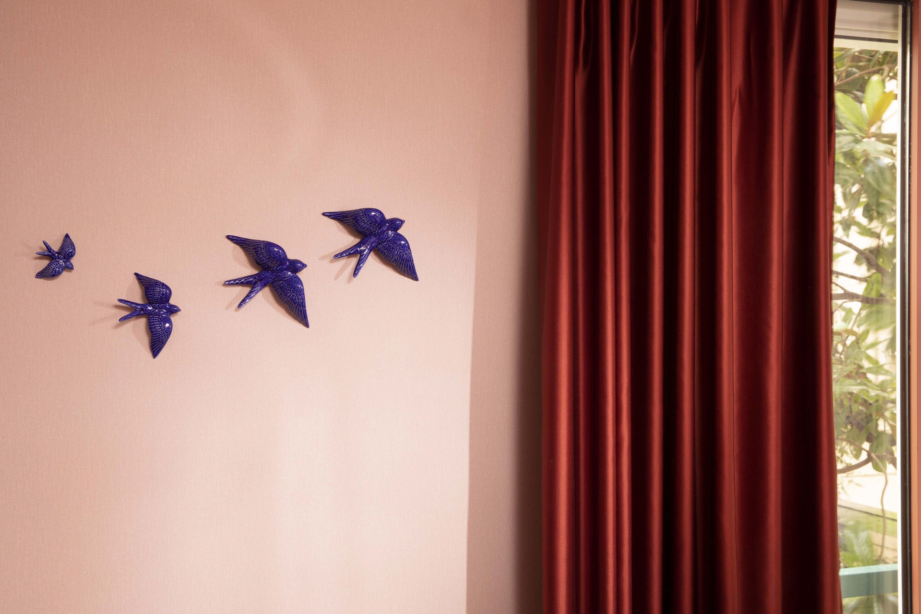 A wall with four blue bird decorations and a window with red curtains.