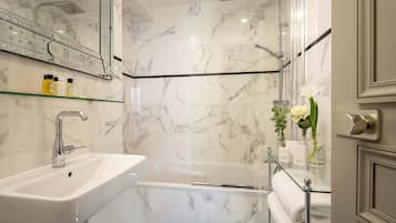 A modern bathroom with a marble sink, glass shower enclosure, and a glass shelf with toiletries.