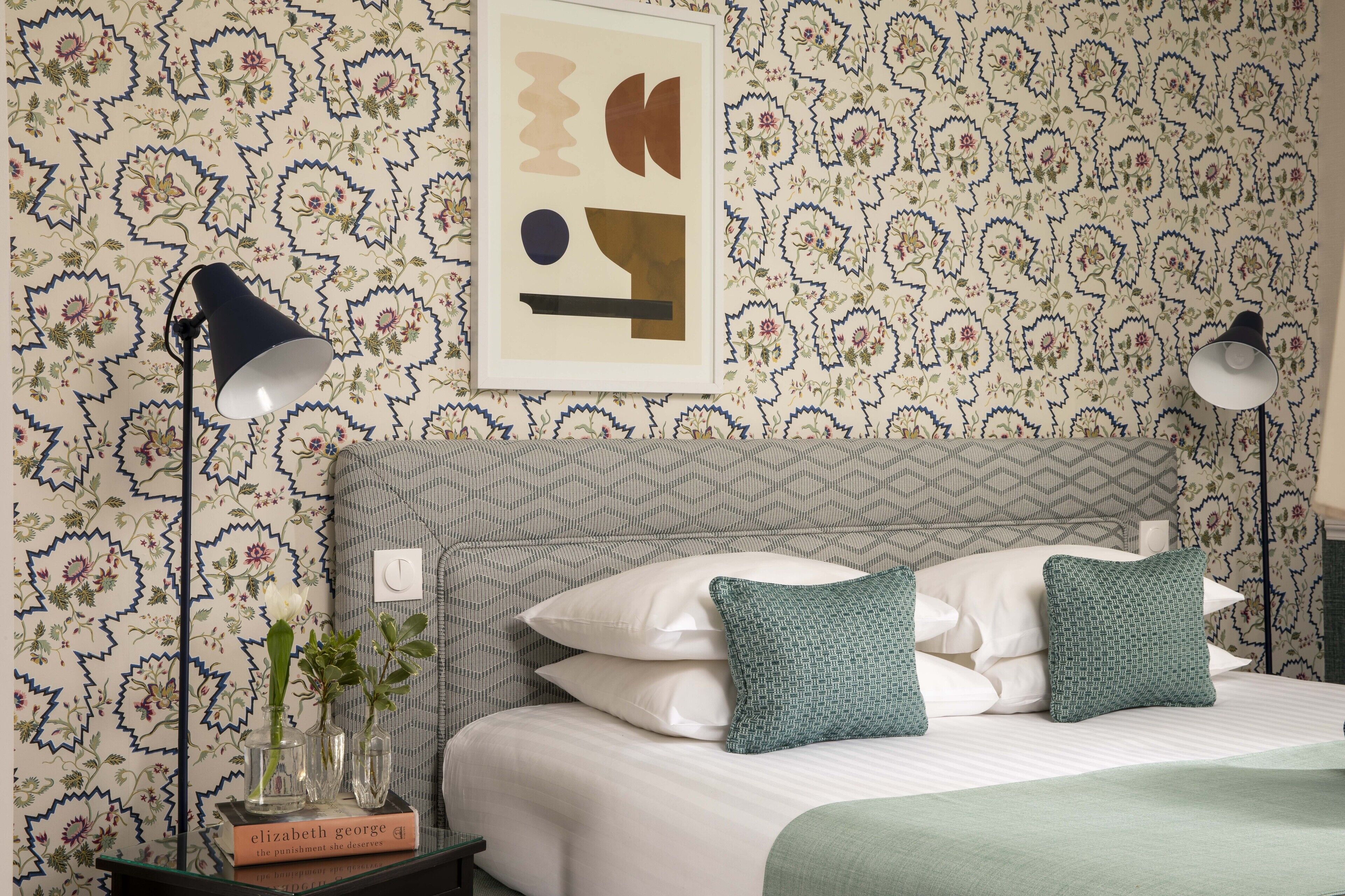 A neatly made bed with white linens and green pillows, a framed abstract artwork on the wall, and a book titled 'Elizabeth George' on a bedside table.