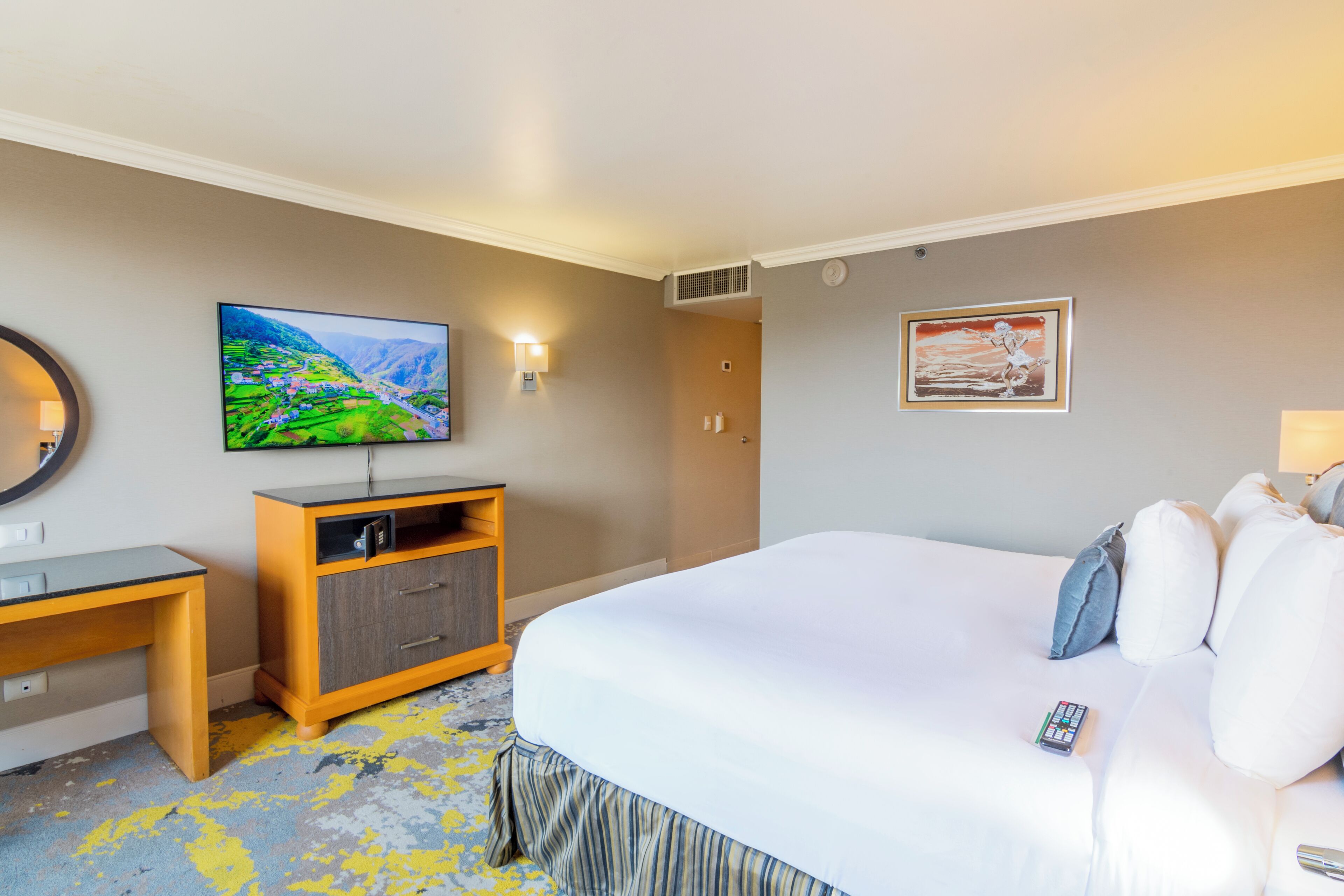 A hotel room with a bed, a desk, a television, and a painting on the wall.