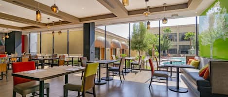 A spacious indoor area with multiple seating arrangements, including tables and chairs, and a large window providing a view of the outdoors.