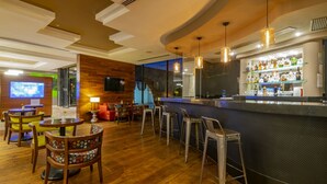 A bar area with wooden flooring, bar stools, a counter with a glass display, and a television screen. - Hotel Lucerna Ciudad Juarez (Ciudad Juárez)