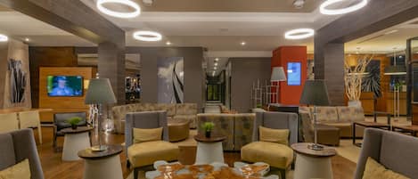 Um lobby moderno com sofás, uma mesa de centro e uma tela de televisão.