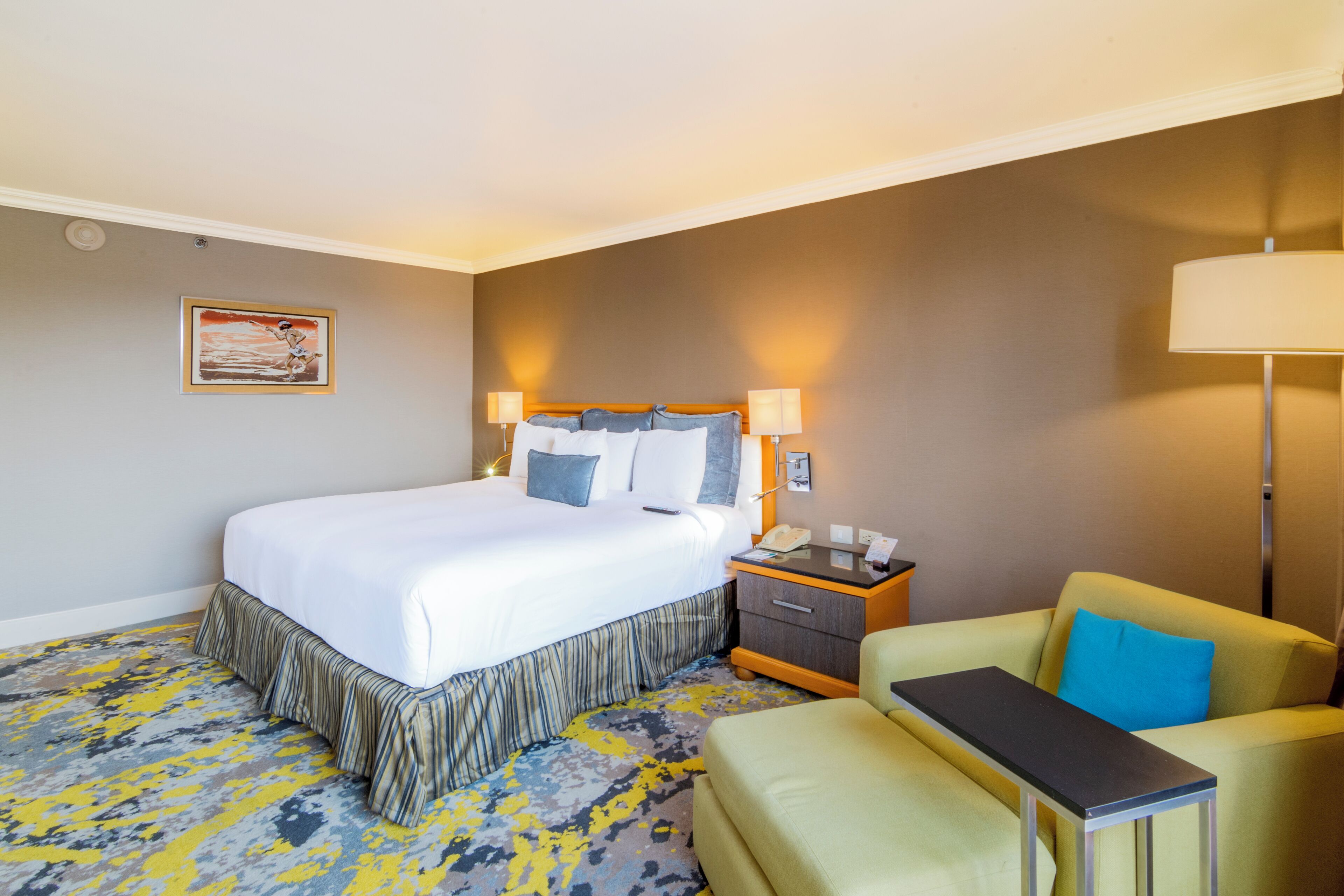 Una habitación de hotel con una cama, mesita de noche, lámpara y una silla.