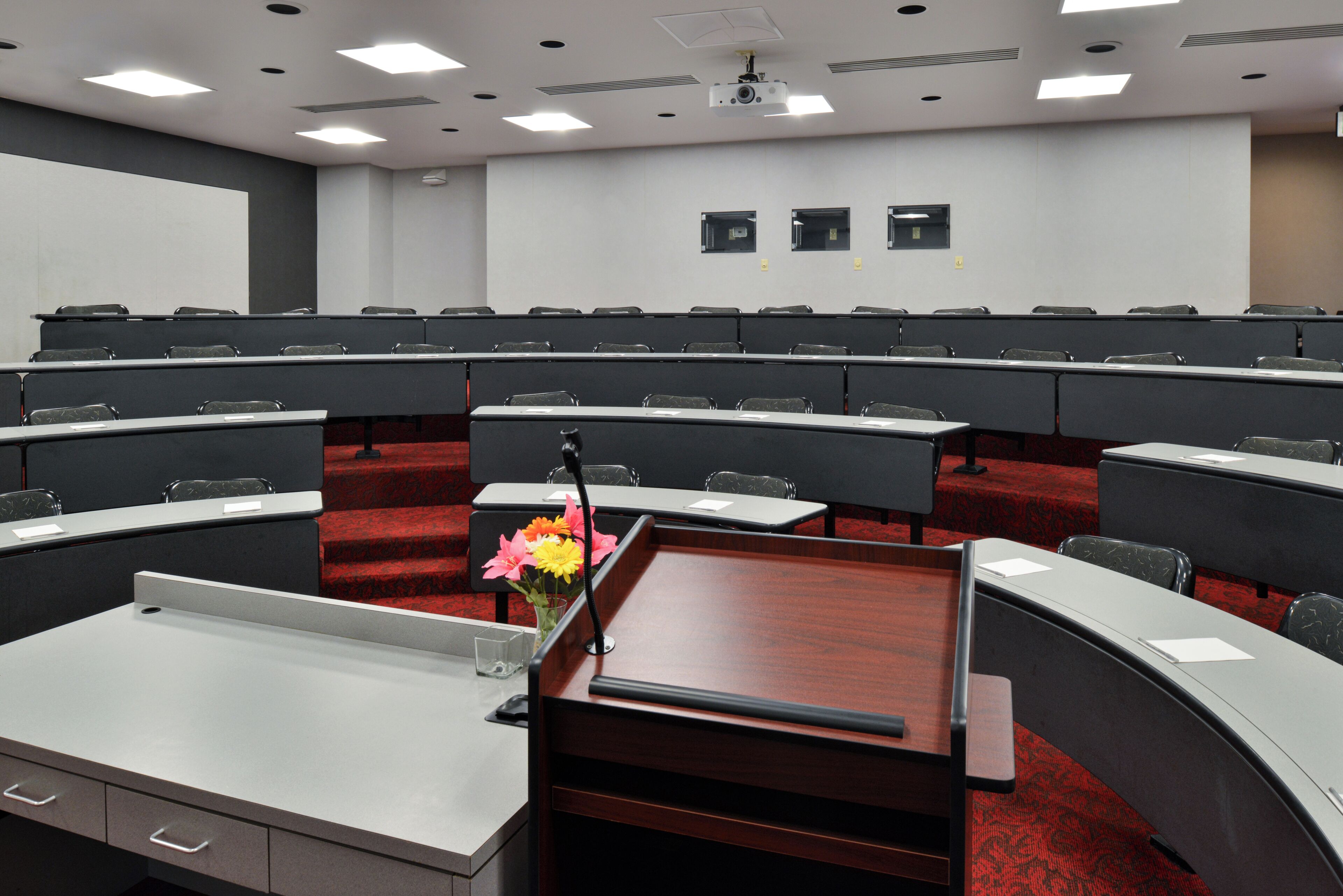 A conference room with a central table, rows of chairs, a projector, and a whiteboard.