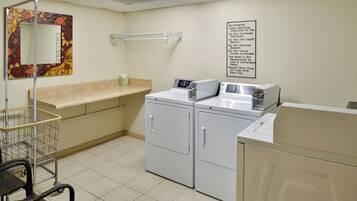 A laundry room with a washing machine, dryer, and a cart.