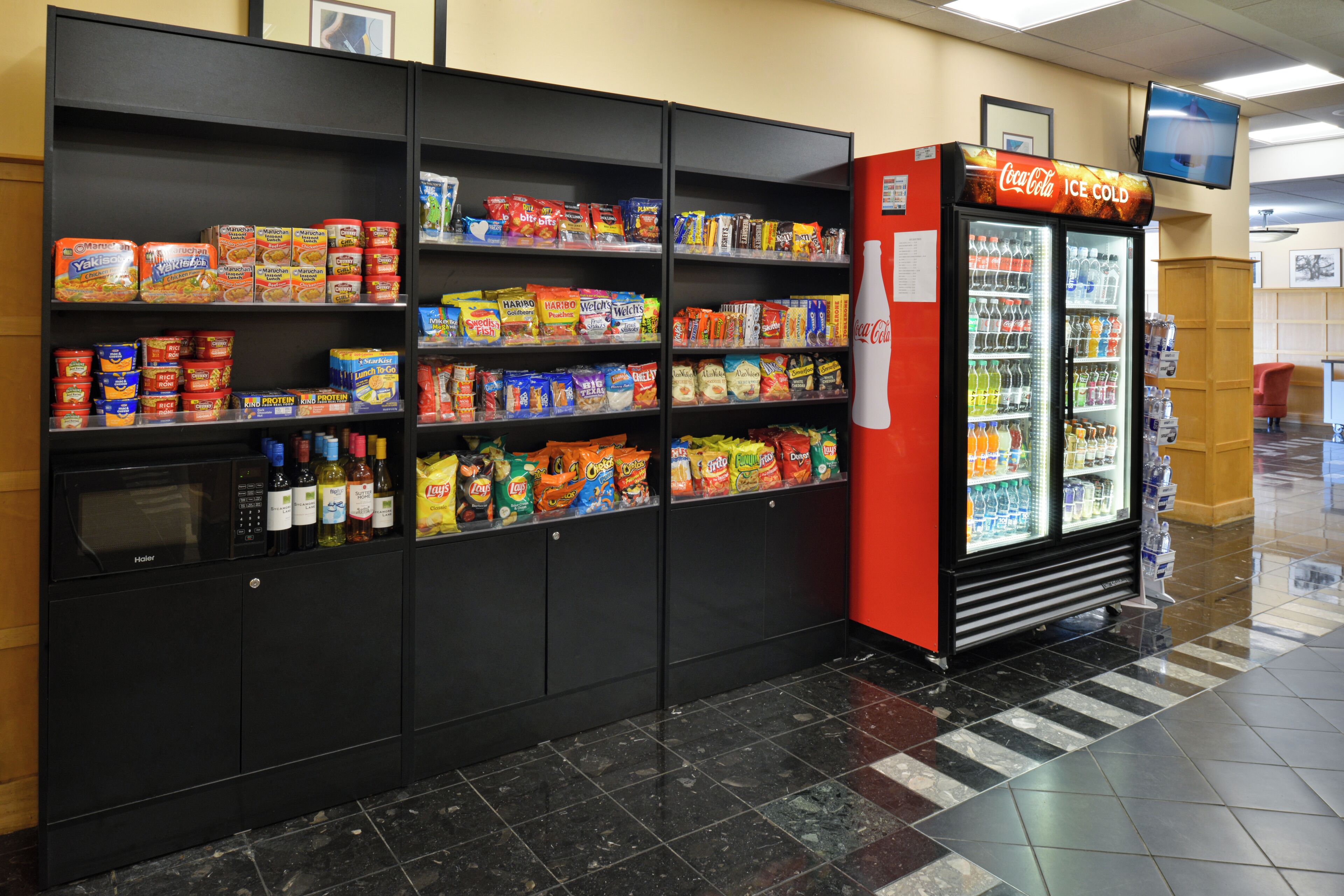 A vending machine stocked with snacks and beverages, a microwave, and a Coca-Cola refrigerator in a public area.