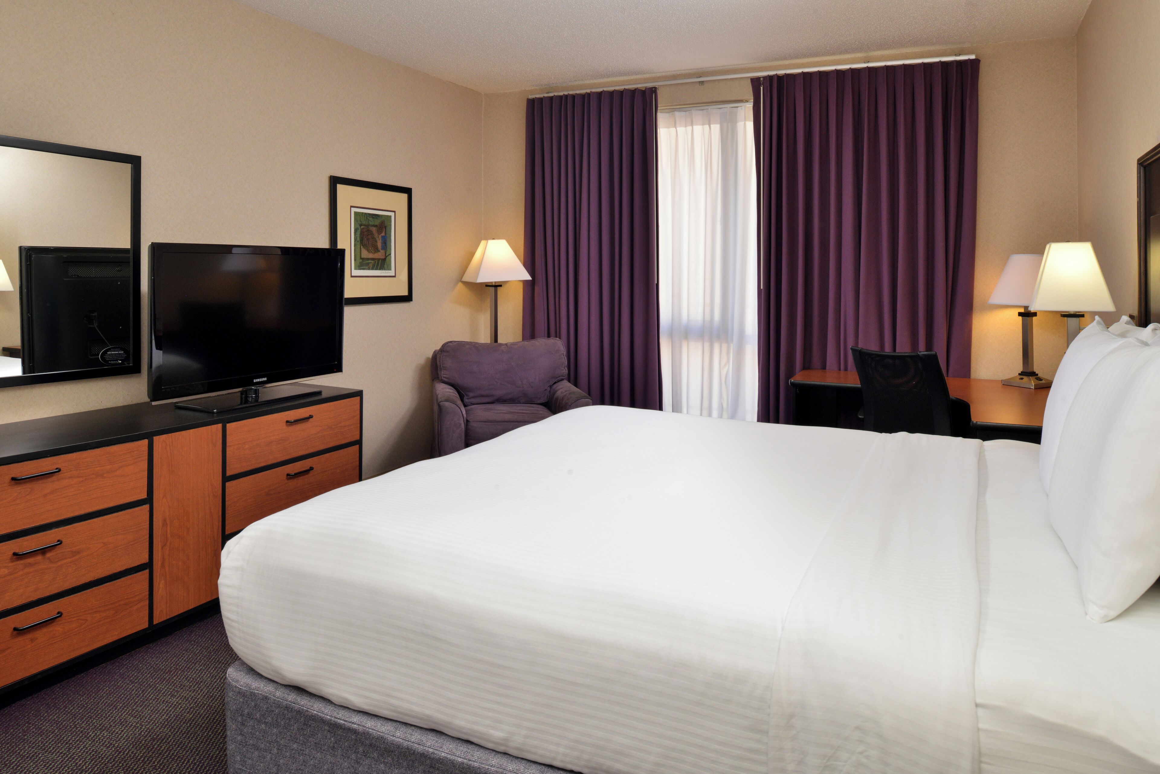 Una habitación de hotel con una cama grande, un televisor de pantalla plana, un escritorio con una silla y dos lámparas.