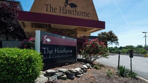 A sign for The Hawthorne Inn & Conference Center with a bird logo, surrounded by landscaping and a clear sky. - Hawthorne Inn and Conference Center (Winston-Salem)