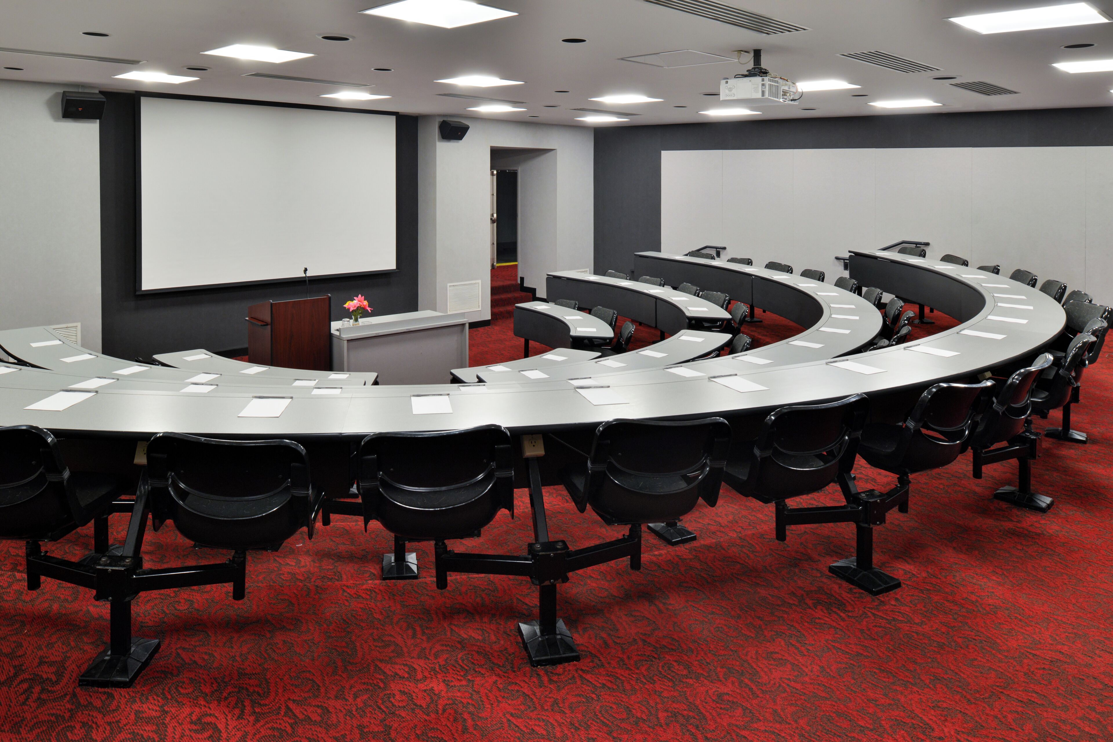 Une salle de conférence équipée d’une table incurvée, de chaises, d’un pupitre et d’un écran de projection.