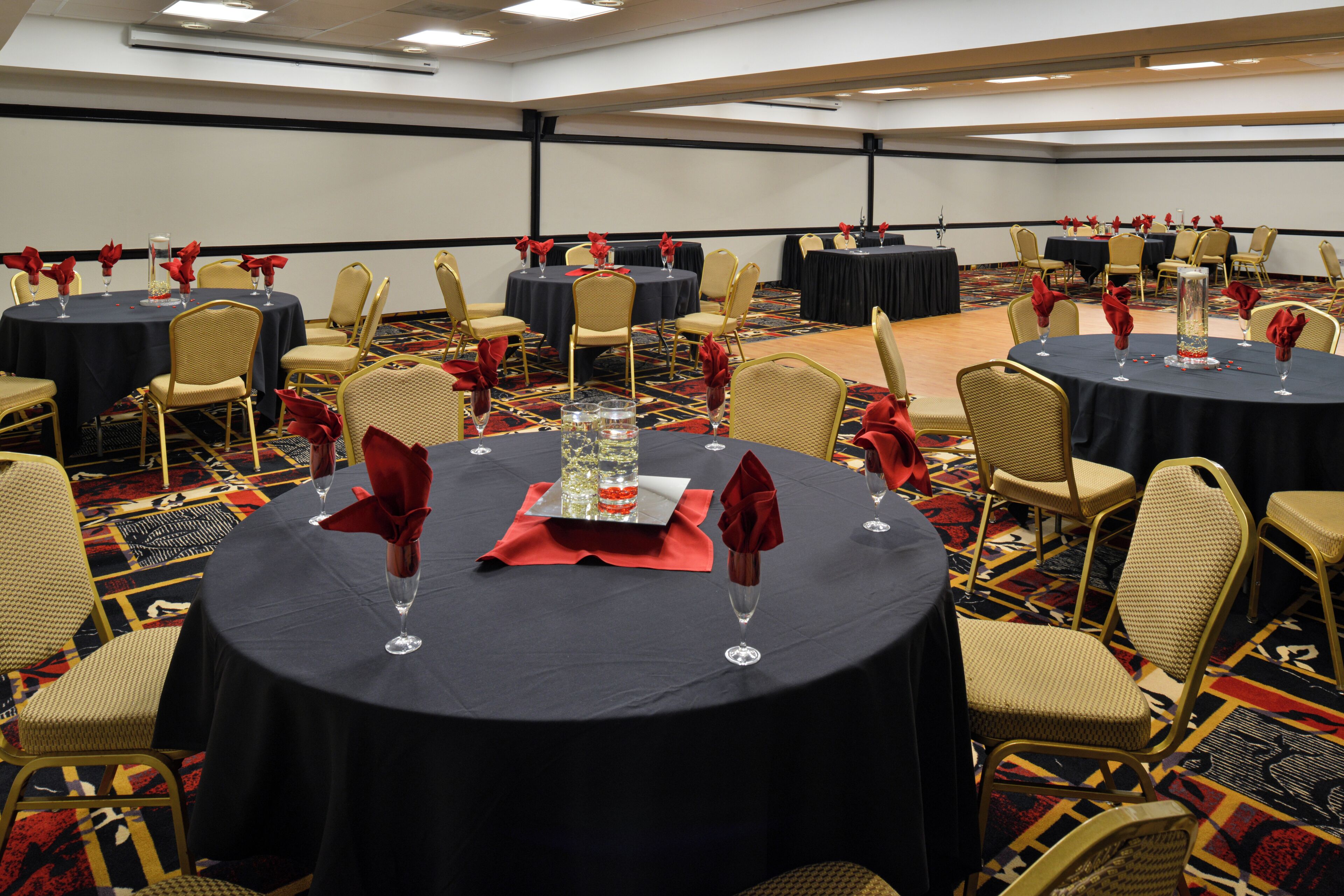 Un salón de conferencias con mesas redondas, sillas y servilletas rojas.