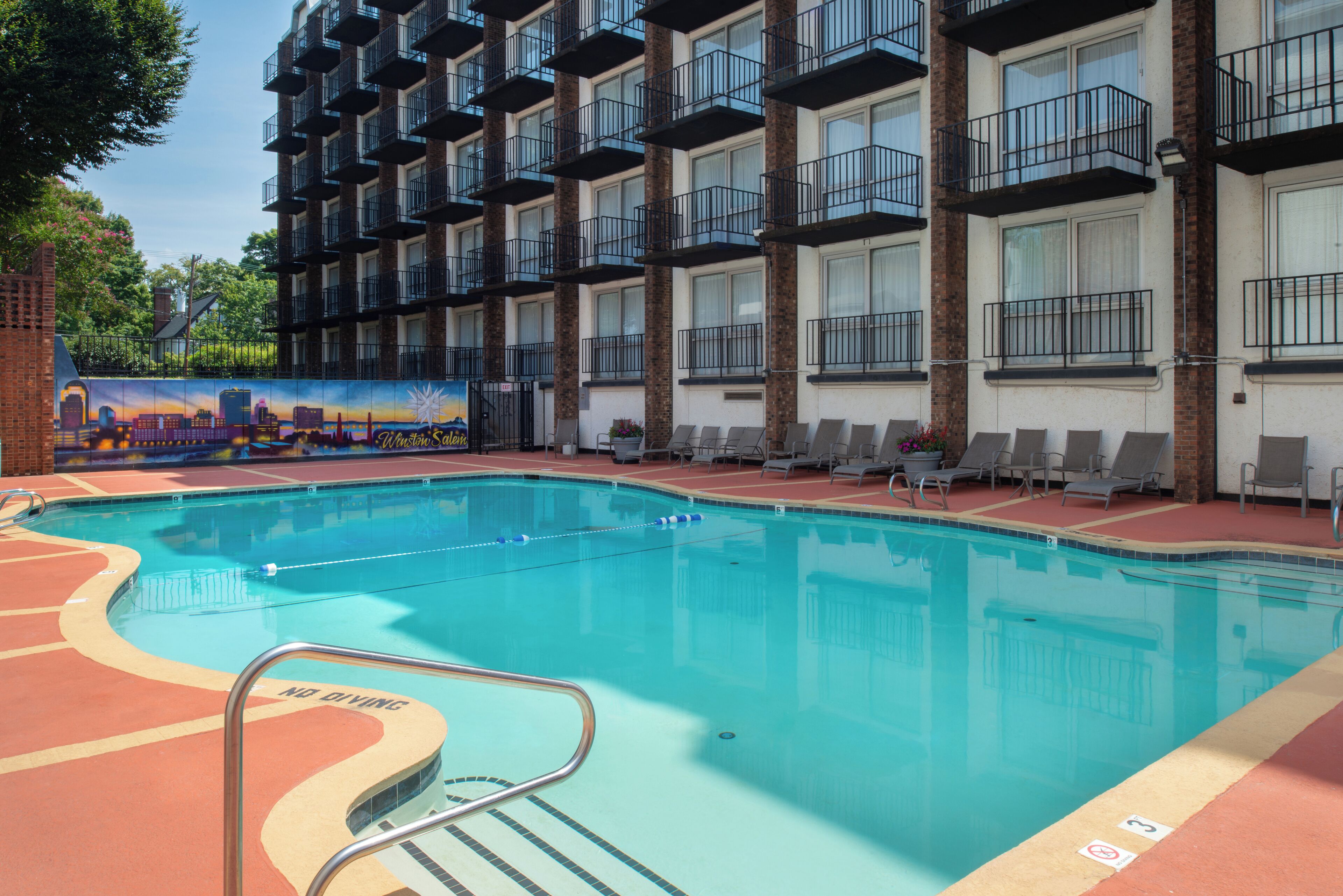 Una piscina con sillones de descanso y un mural en el edificio.
