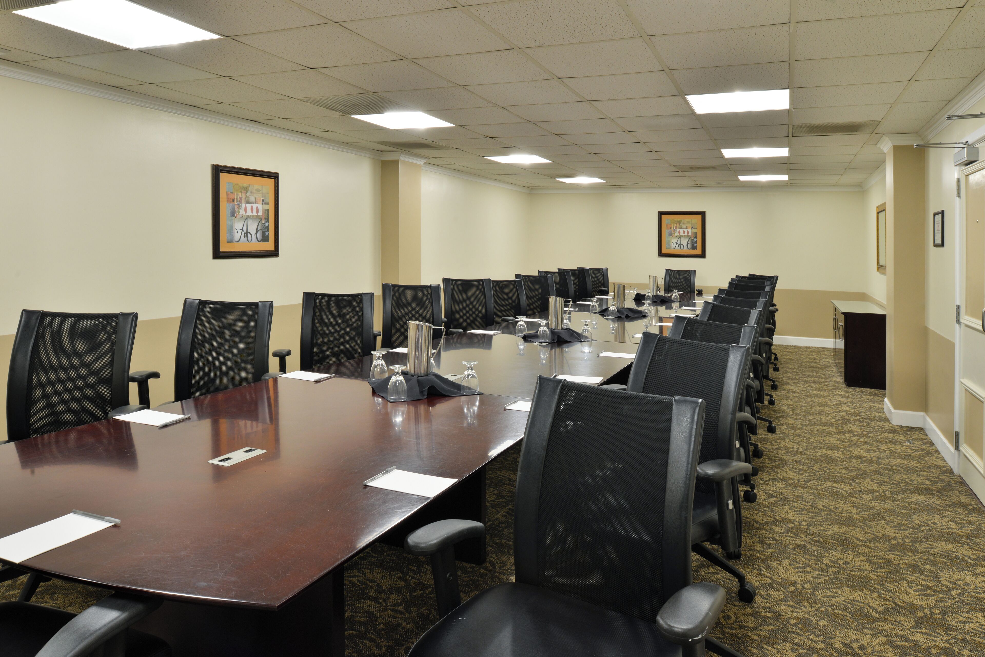 A conference room with a long table, multiple chairs, and framed pictures on the walls.