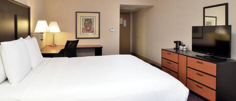 A hotel room with a large bed, a desk with a lamp, a television, and a dresser.