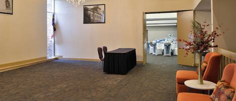 A spacious room with a carpeted floor, a chandelier, a table with chairs, and a seating area with a small table and a vase of flowers.