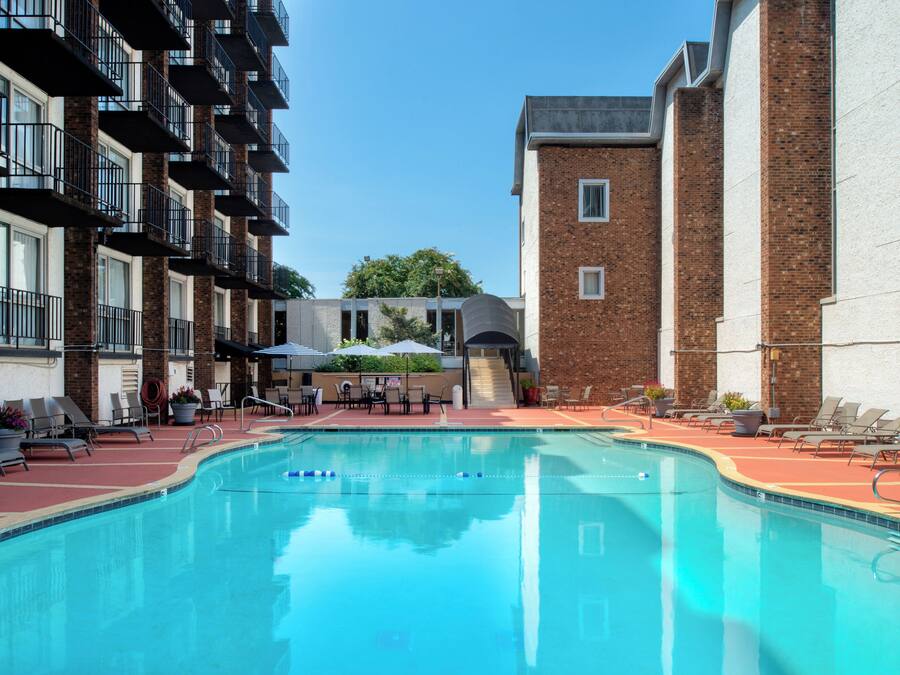 A swimming pool with lounge chairs and umbrellas, surrounded by brick buildings with balconies.