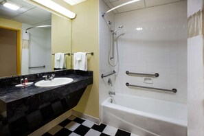 Um banheiro com chão quadriculado em preto e branco, uma banheira branca, uma pia com bancada de mármore preto e um espelho com porta-toalhas.