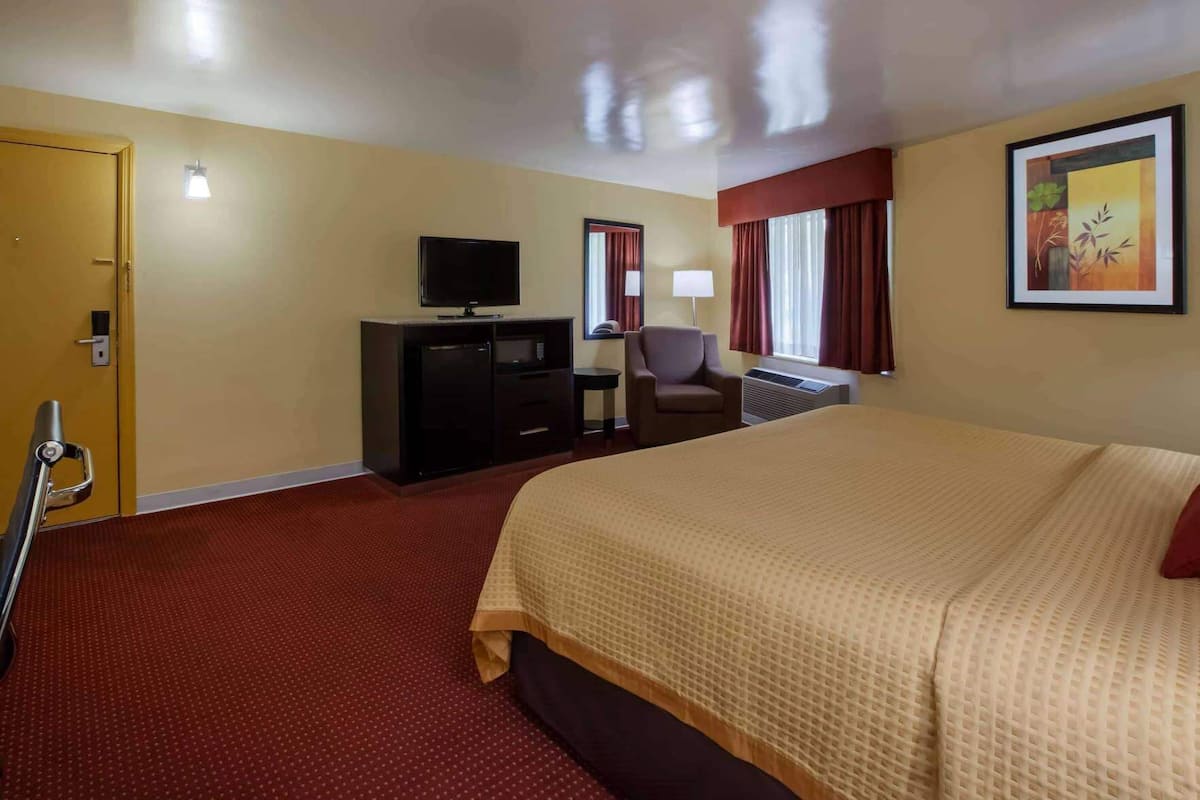 Une chambre d’hôtel avec un grand lit, une télévision, un bureau avec une chaise et une fenêtre avec des rideaux.