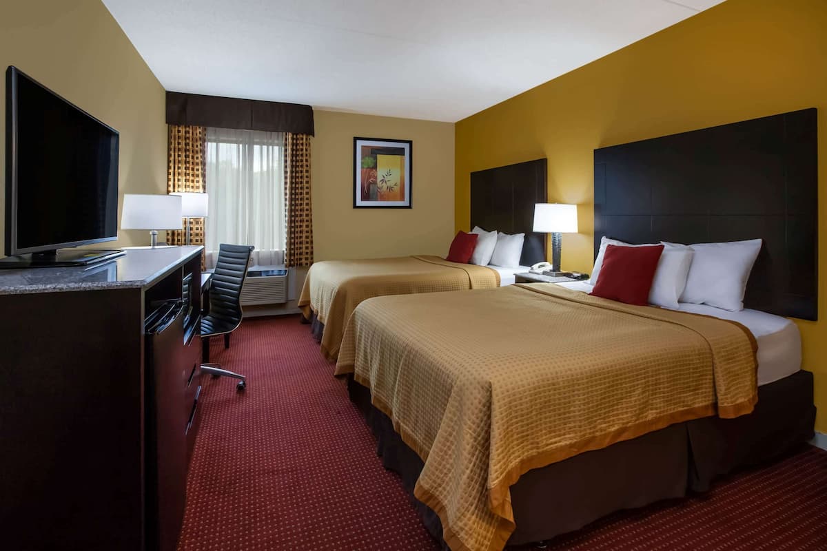 Une chambre d’hôtel avec deux lits, un bureau avec une télévision et une moquette rouge.