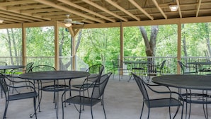 An outdoor patio with round tables and chairs, surrounded by a wooden pergola with a ceiling fan.