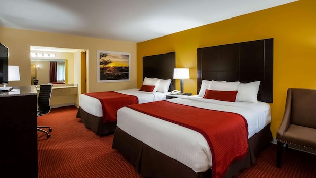 A hotel room with two beds, a desk, a chair, and a painting on the wall.