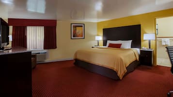 A hotel room with a large bed, two bedside tables, a desk with a computer, a TV, and a window with curtains.