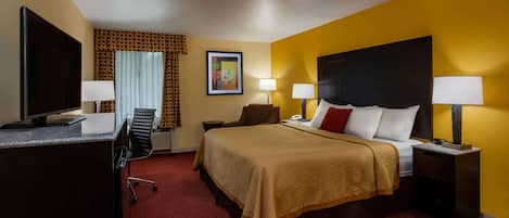 A hotel room with a bed, two bedside tables with lamps, a desk with a flat-screen TV, a chair, a red carpet, and a window with curtains.