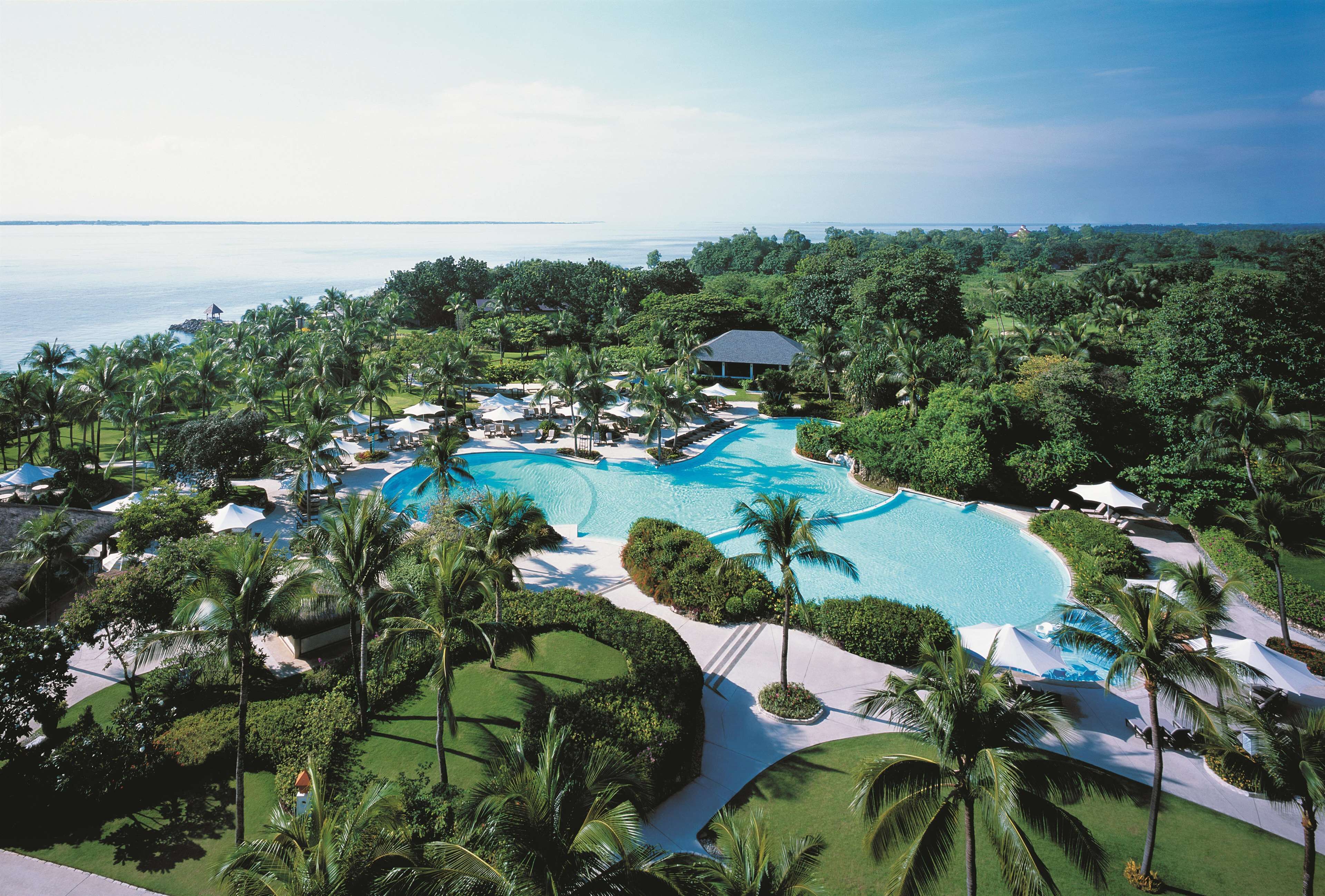 Ein Resort mit großem Pool, umgeben von Palmen und Blick auf den Ozean.