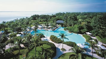 Un resort con una piscina grande rodeada de palmeras y vistas al océano.