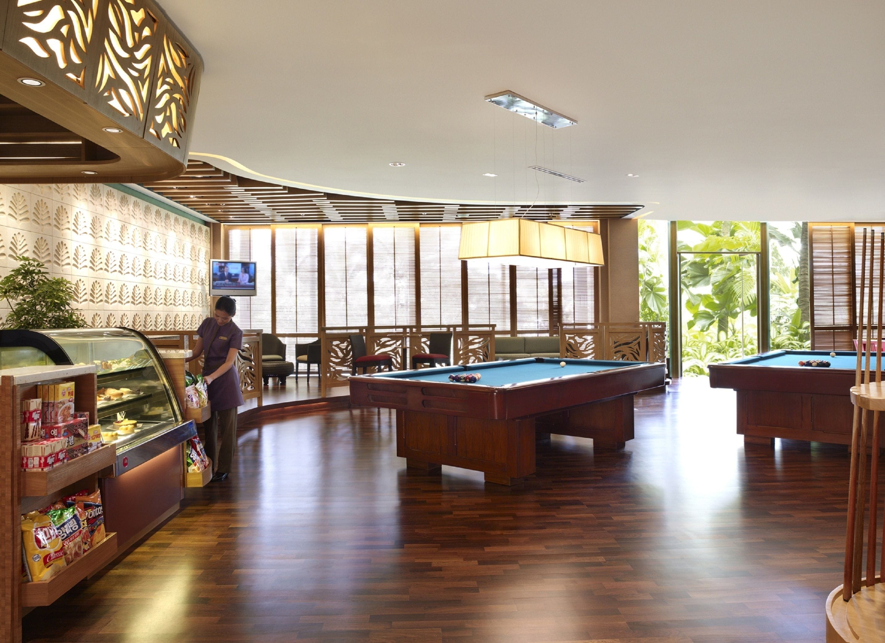 A pool area with wooden pool tables, a snack bar, and a television screen.