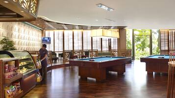 A pool area with wooden pool tables, a snack bar, and a television screen.