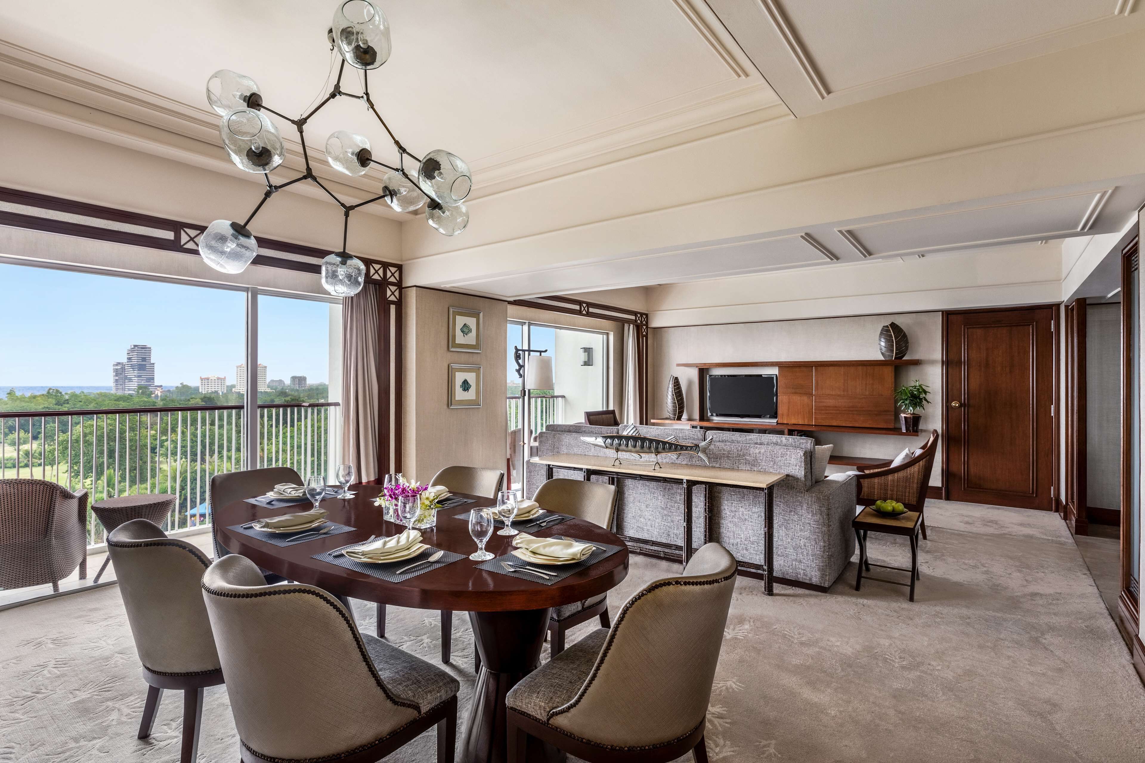 A dining area with a round table set for six, a bar area with a sofa, and a city view through large windows.