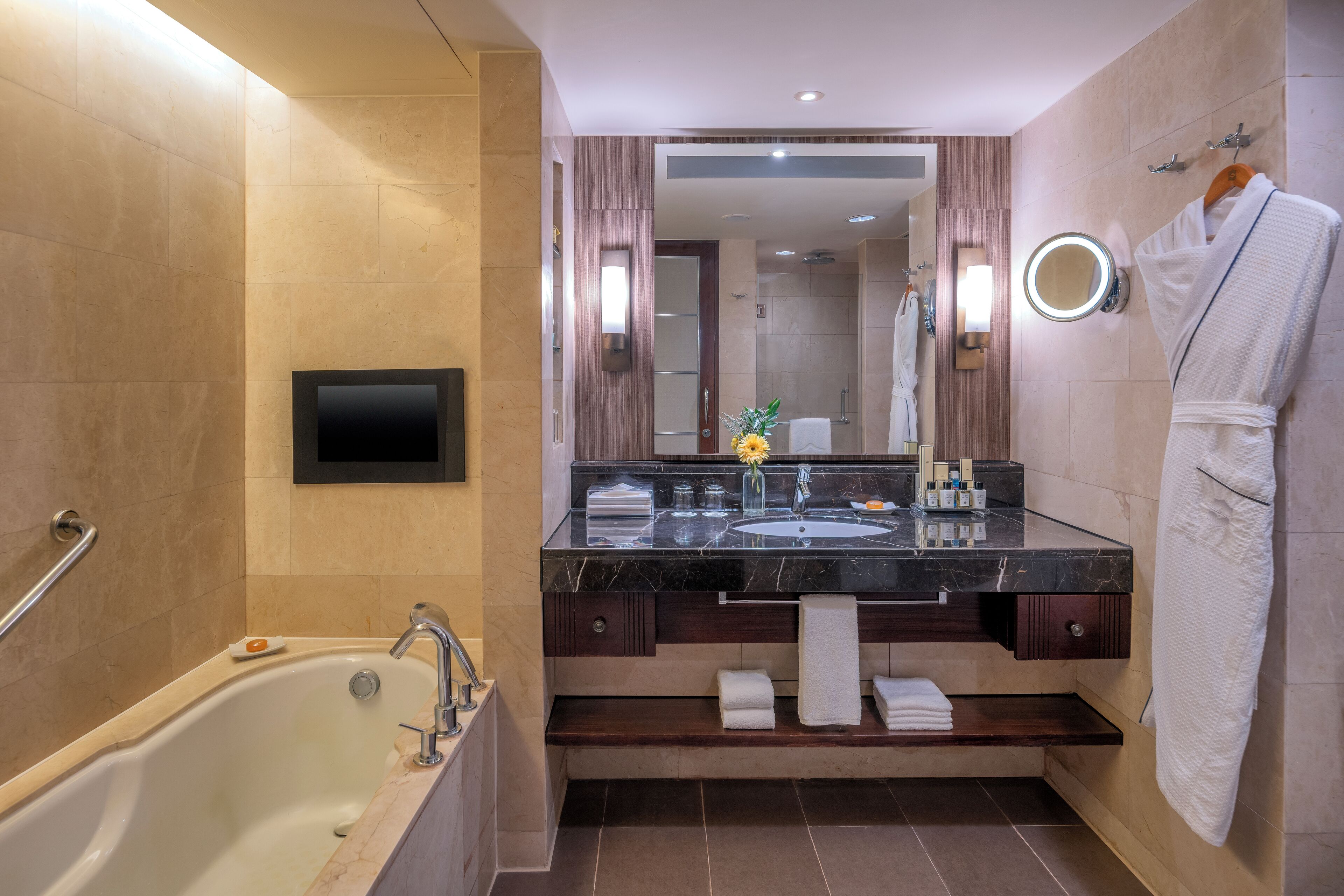 A modern bathroom with a bathtub, a vanity with a glass countertop, a mirror, and a robe hanging on a rack.