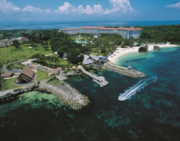 An aerial view of a resort with a large building, a beach, and clear blue waters. - Shangri-La Mactan, Cebu (Lapu-Lapu)