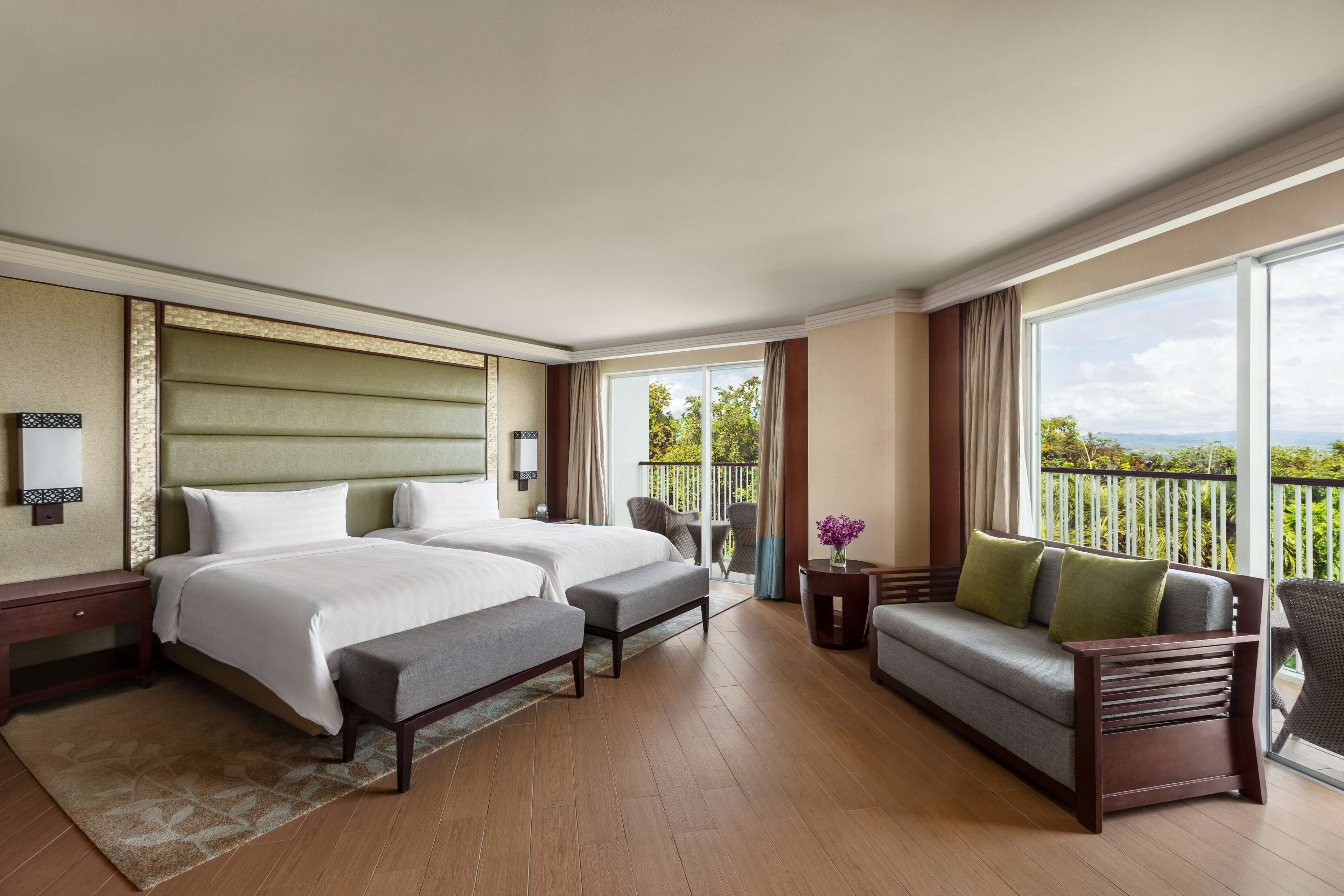 A hotel room with two beds, a sofa, a small table, and a balcony with a view.
