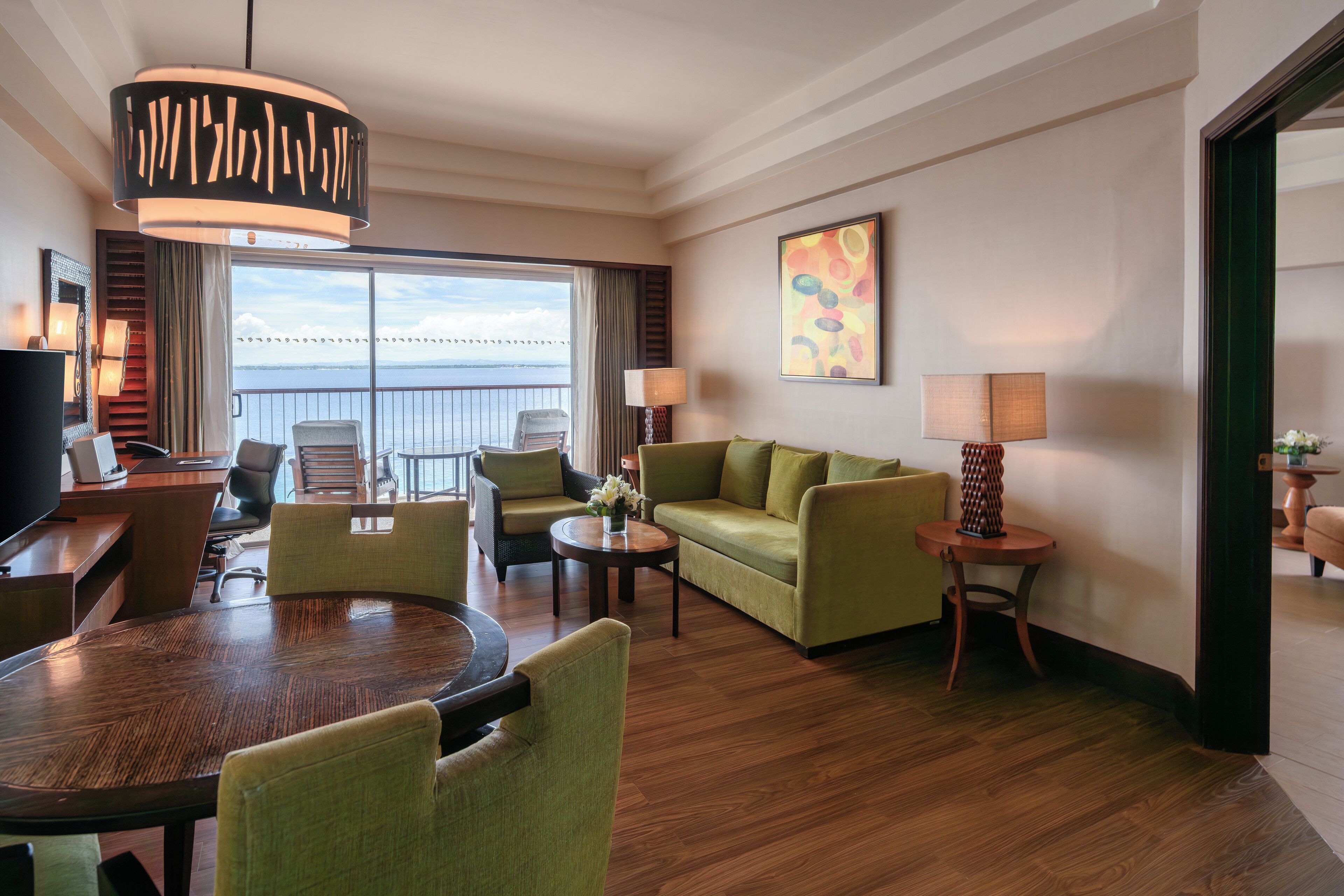 A hotel room with a balcony, a sofa, a dining table, and a TV.