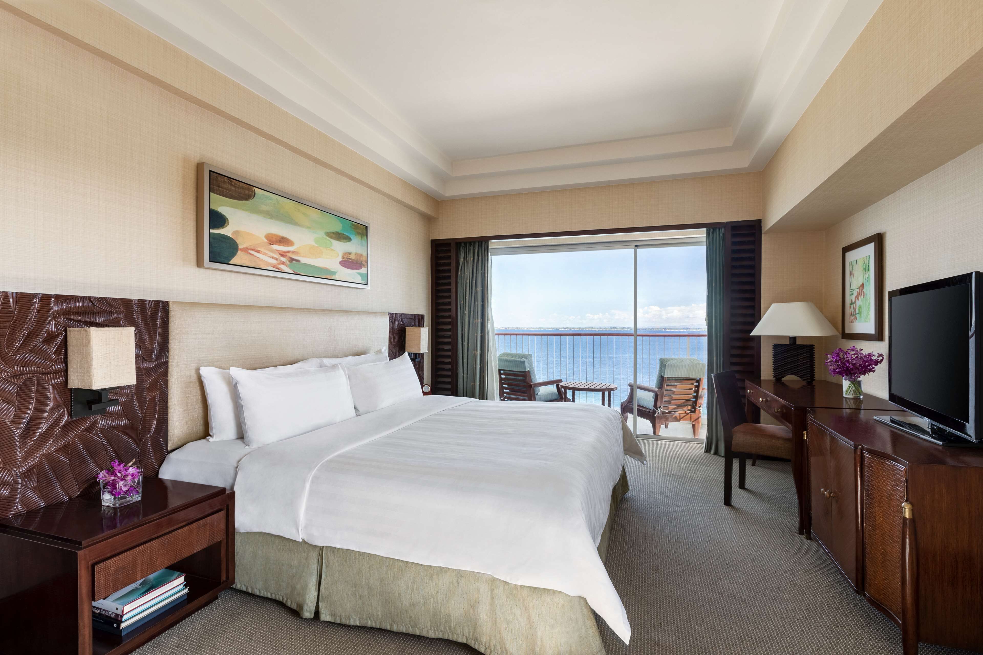 Habitación de hotel con una cama grande, un escritorio con lámpara, televisión y vista al mar.