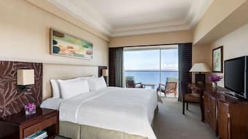 Habitación de hotel con una cama grande, un escritorio con lámpara, televisión y vista al mar.