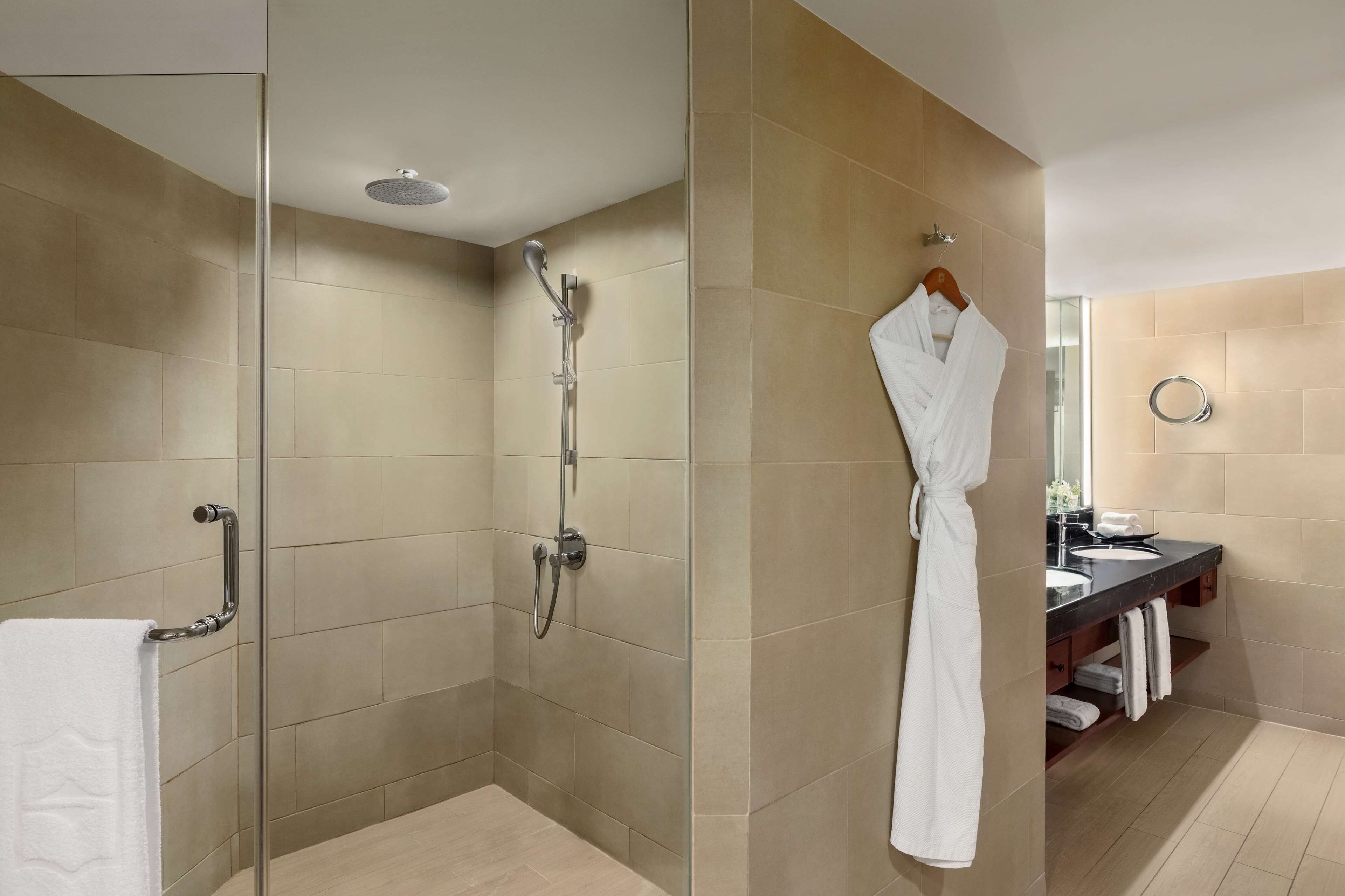 A modern bathroom with a glass-enclosed shower, a vanity with a mirror, and a robe hanging on a rack.