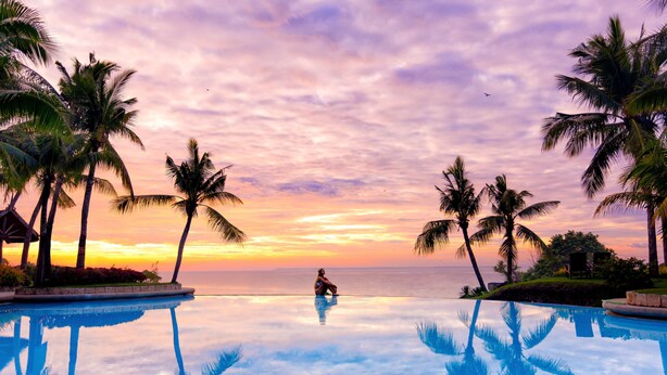 A pool with a sunset view, palm trees, and a person sitting by the pool. - Shangri-La Mactan, Cebu (Lapu-Lapu)