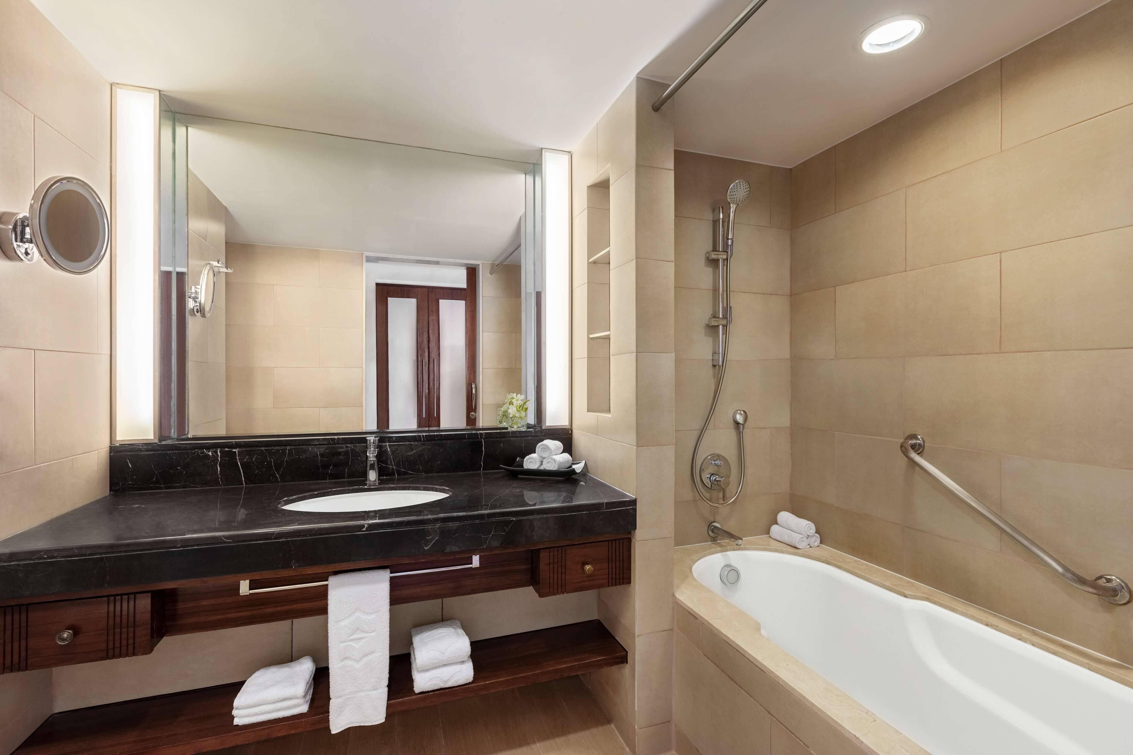 A modern bathroom with a black marble sink, a large mirror, a bathtub, and a shower with a handheld showerhead.